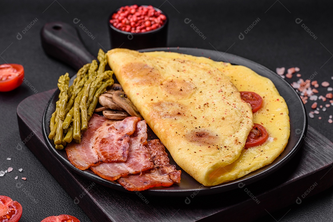 Deliciosa omelete fresca com tomate cereja, bacon, aspargos e especiarias sobre um fundo escuro de concreto