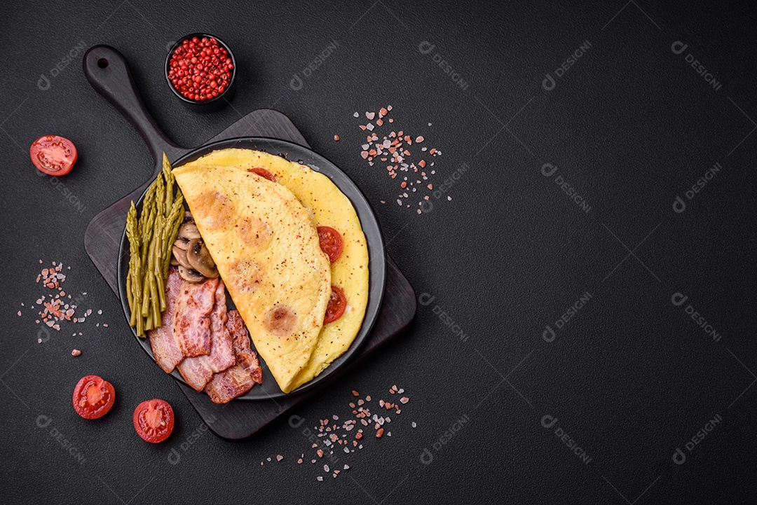 Deliciosa omelete fresca com tomate cereja, bacon, aspargos e especiarias sobre um fundo escuro de concreto