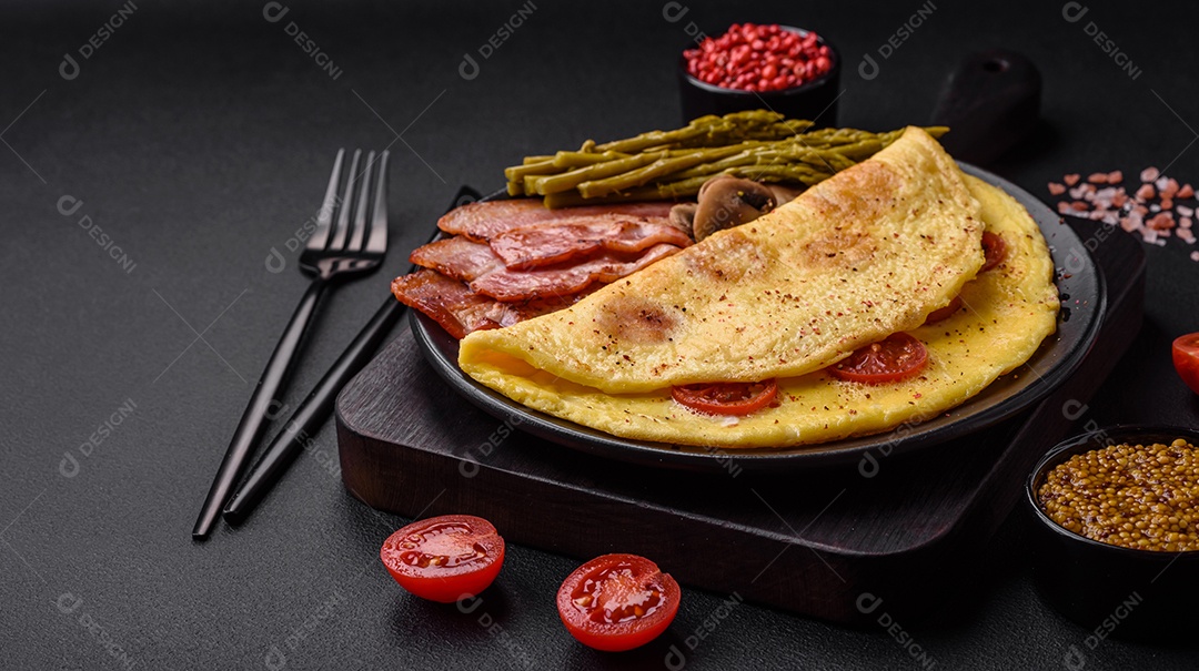 Deliciosa omelete fresca com tomate cereja, bacon, aspargos e especiarias sobre um fundo escuro de concreto