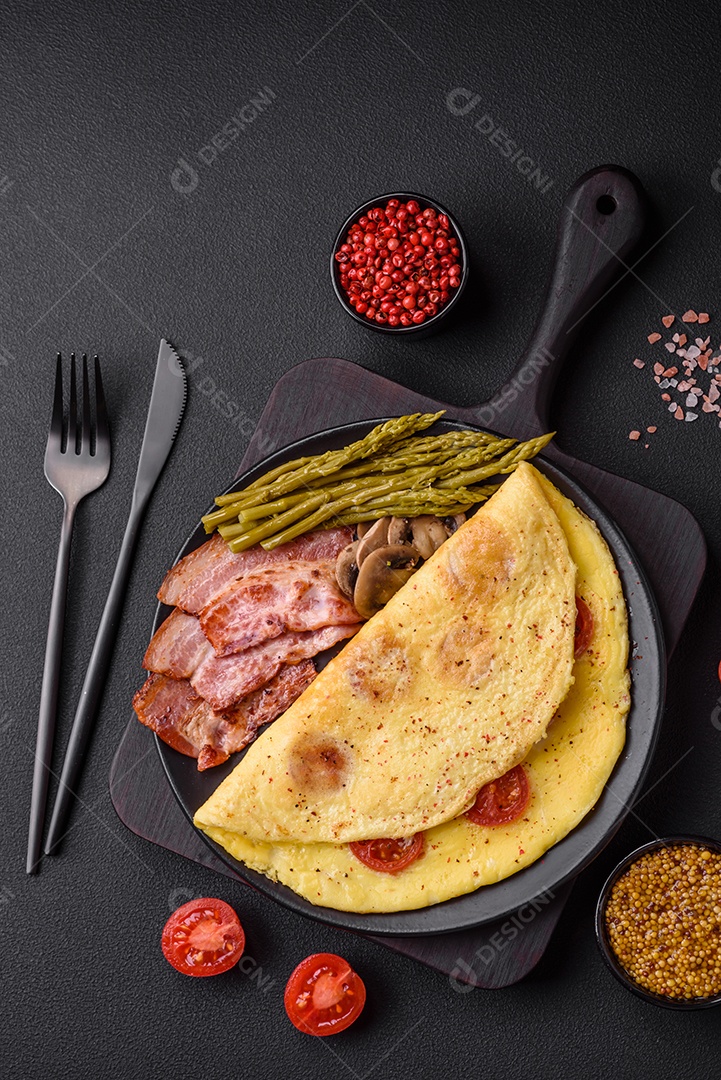 Deliciosa omelete fresca com tomate cereja, bacon, aspargos e especiarias sobre um fundo escuro de concreto