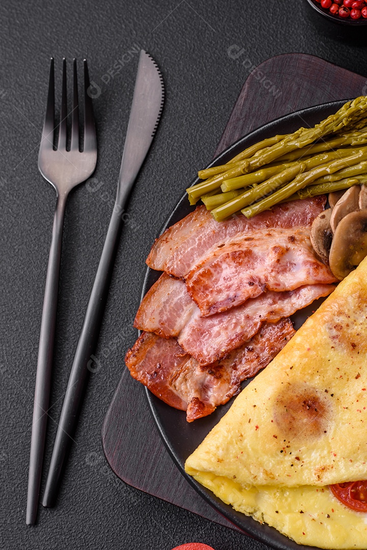 Deliciosa omelete fresca com tomate cereja, bacon, aspargos e especiarias sobre um fundo escuro de concreto