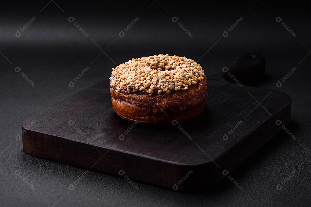 Delicioso donut com recheio de creme e nozes em um fundo escuro de concreto. Comida doce