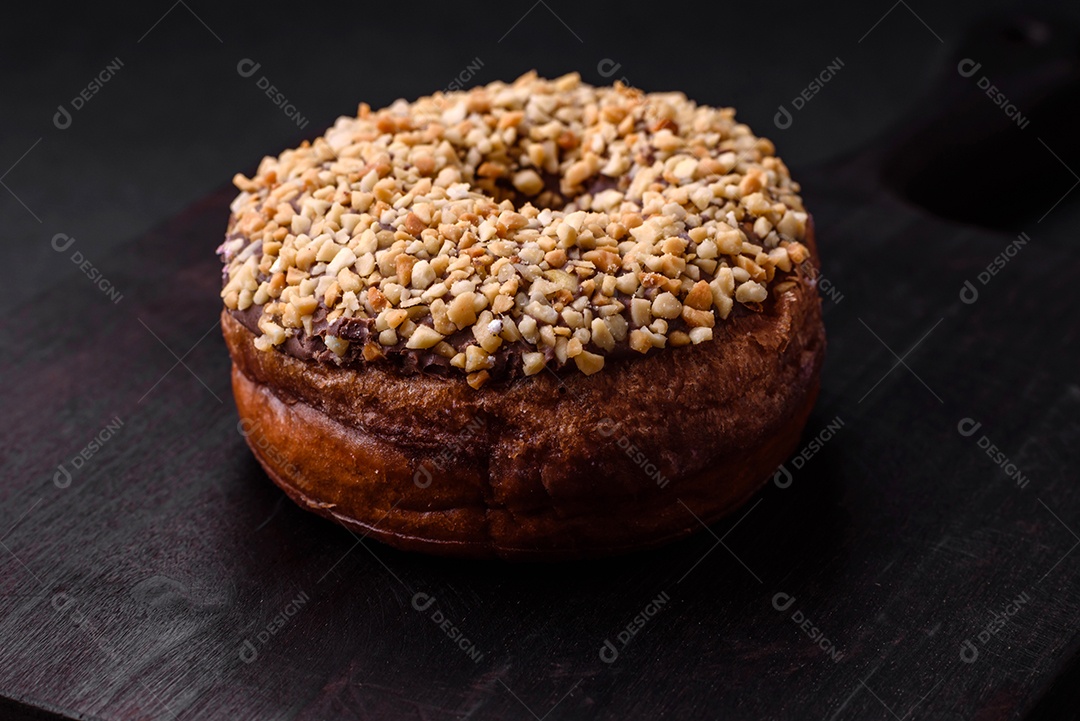 Delicioso donut com recheio de creme e nozes em um fundo escuro de concreto. Comida doce