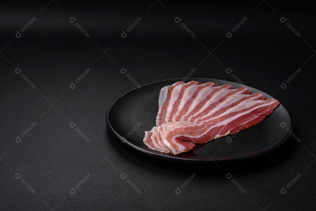 Deliciosa pancetta fresca com sal e especiarias cortadas em fatias finas sobre um fundo escuro de concreto