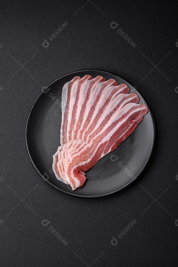 Deliciosa pancetta fresca com sal e especiarias cortadas em fatias finas sobre um fundo escuro de concreto