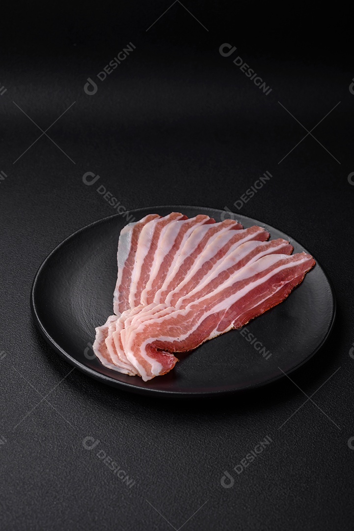 Deliciosa pancetta fresca com sal e especiarias cortadas em fatias finas sobre um fundo escuro de concreto