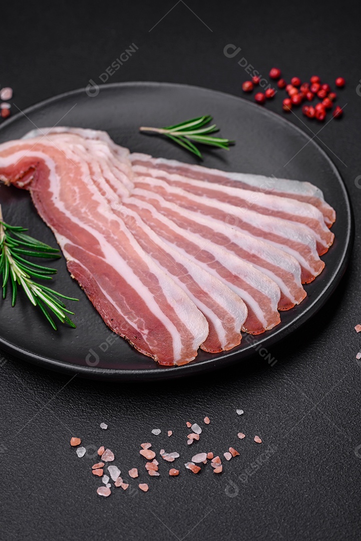 Deliciosa pancetta fresca com sal e especiarias cortadas em fatias finas sobre um fundo escuro de concreto