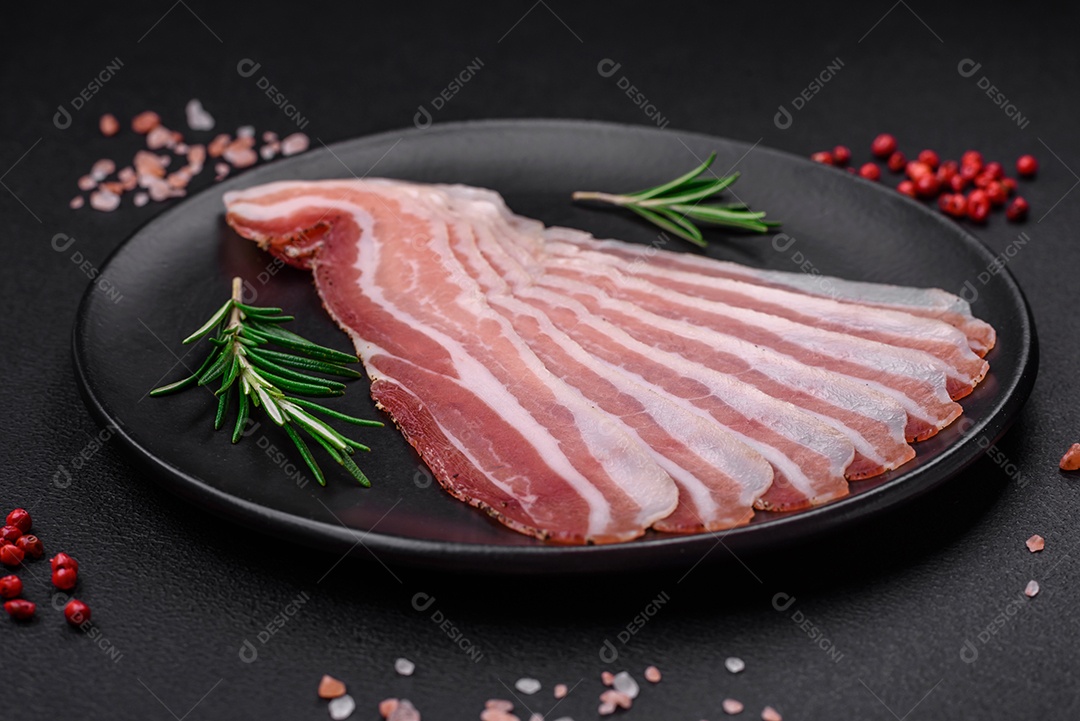 Deliciosa pancetta fresca com sal e especiarias cortadas em fatias finas sobre um fundo escuro de concreto