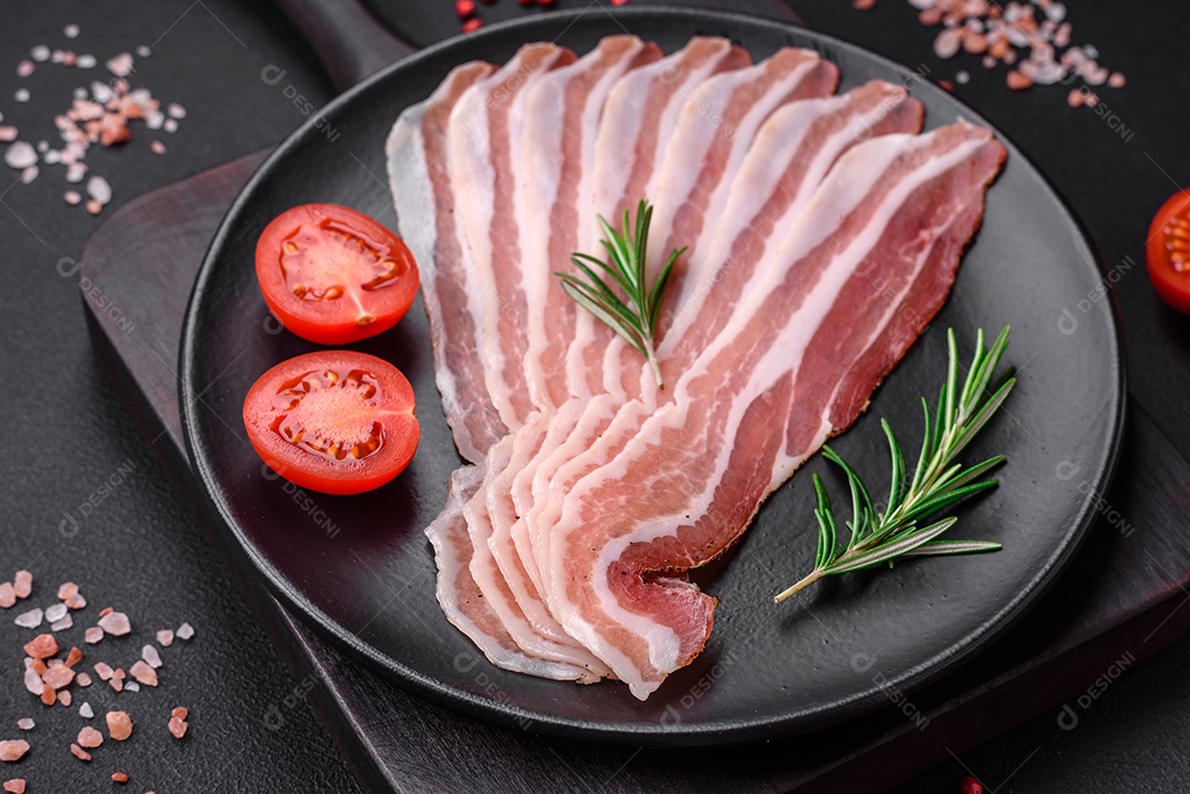 Deliciosa pancetta fresca com sal e especiarias cortadas em fatias finas sobre um fundo escuro de concreto