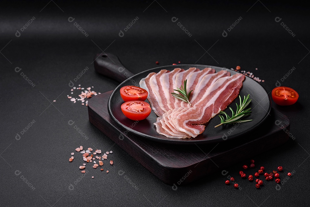 Deliciosa pancetta fresca com sal e especiarias cortadas em fatias finas sobre um fundo escuro de concreto