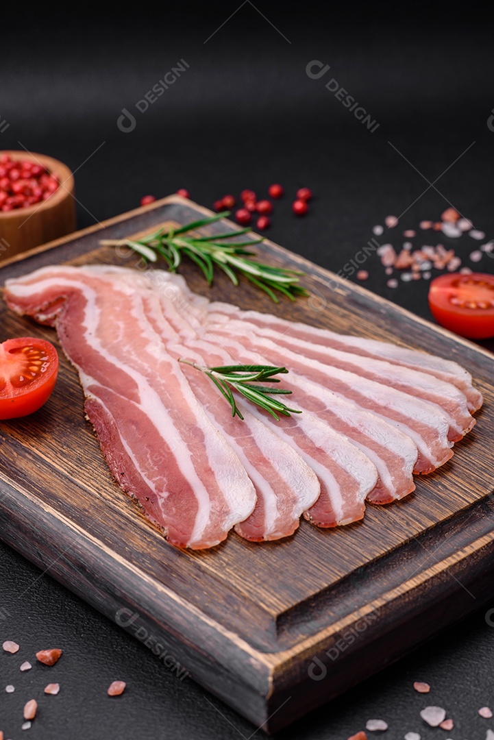 Deliciosa pancetta fresca com sal e especiarias cortadas em fatias finas sobre um fundo escuro de concreto