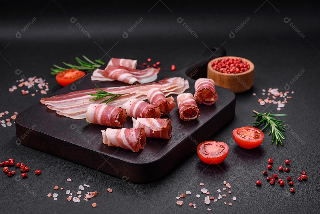 Deliciosa pancetta fresca com sal e especiarias cortadas em fatias finas sobre um fundo escuro de concreto