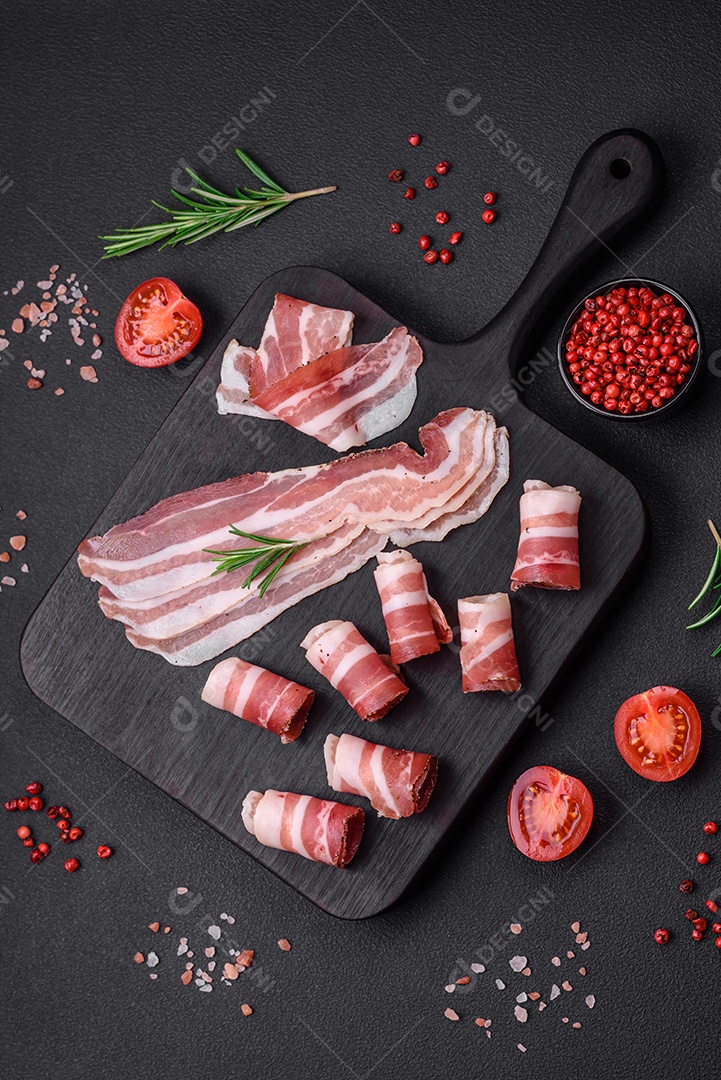 Deliciosa pancetta fresca com sal e especiarias cortadas em fatias finas sobre um fundo escuro de concreto