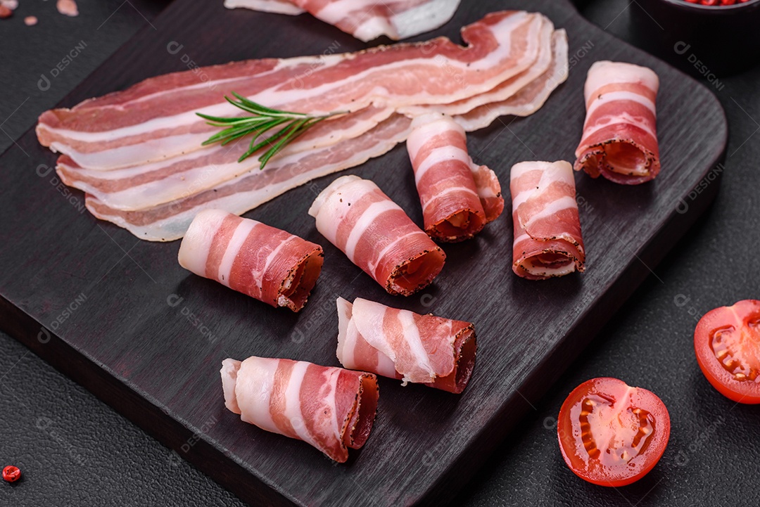 Deliciosa pancetta fresca com sal e especiarias cortadas em fatias finas sobre um fundo escuro de concreto