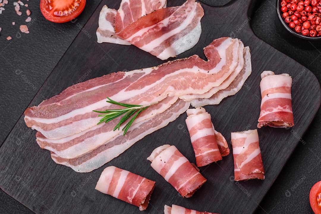 Deliciosa pancetta fresca com sal e especiarias cortadas em fatias finas sobre um fundo escuro de concreto