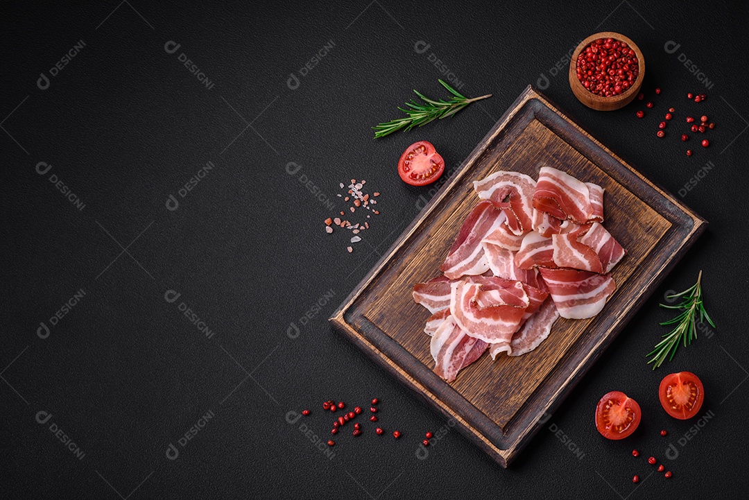 Deliciosa pancetta fresca com sal e especiarias cortadas em fatias finas sobre um fundo escuro de concreto