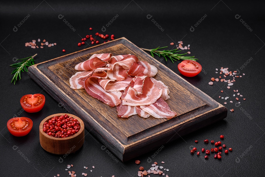 Deliciosa pancetta fresca com sal e especiarias cortadas em fatias finas sobre um fundo escuro de concreto