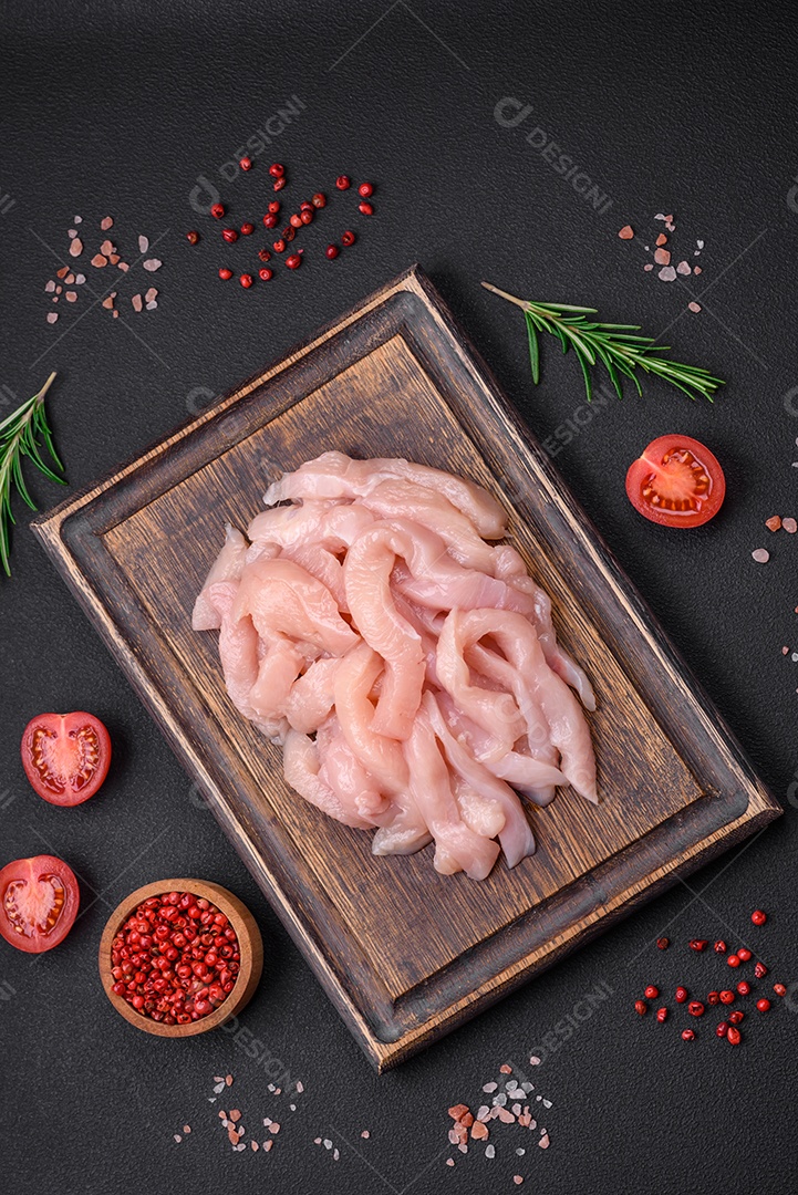 Filé de frango cru cortado em tiras com especiarias e ervas numa tábua de madeira