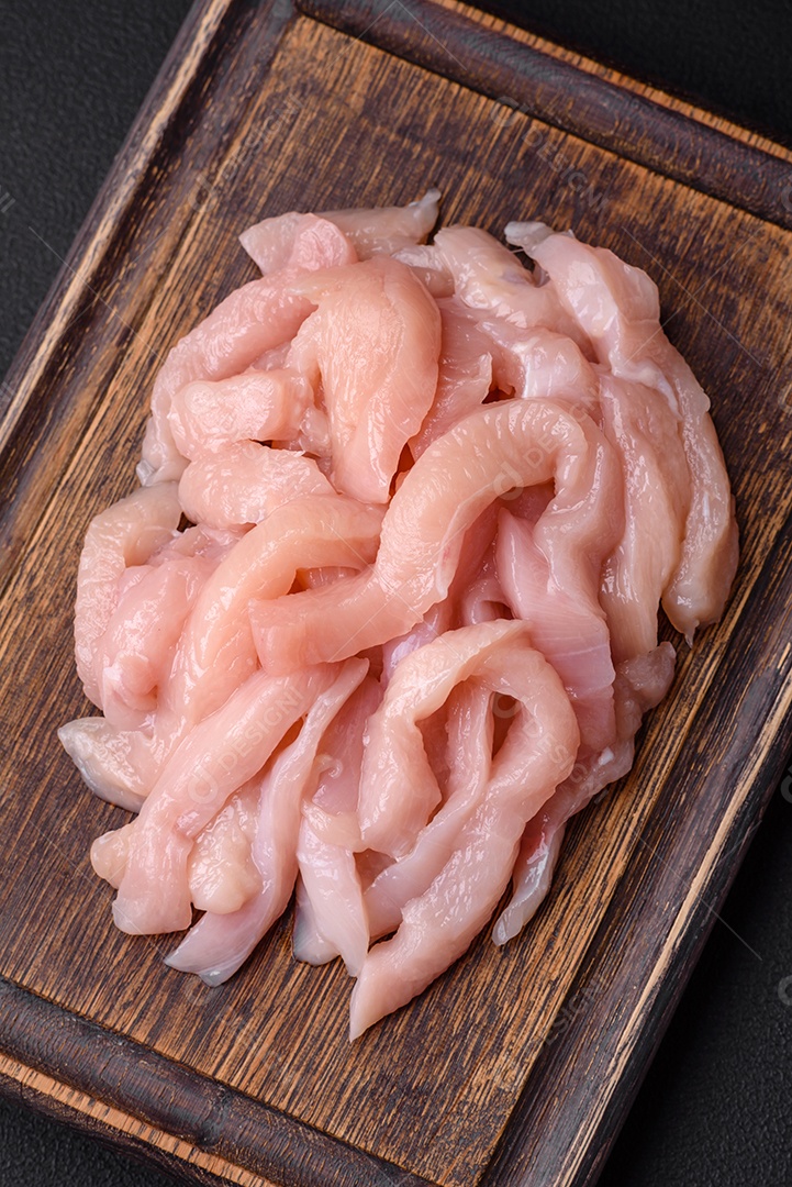 Filé de frango cru cortado em tiras com especiarias e ervas numa tábua de madeira