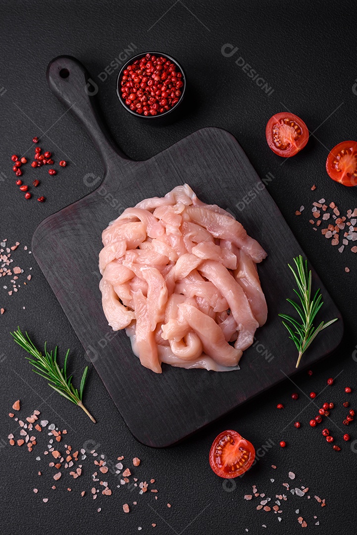 Filé de frango cru cortado em tiras com especiarias e ervas numa tábua de madeira