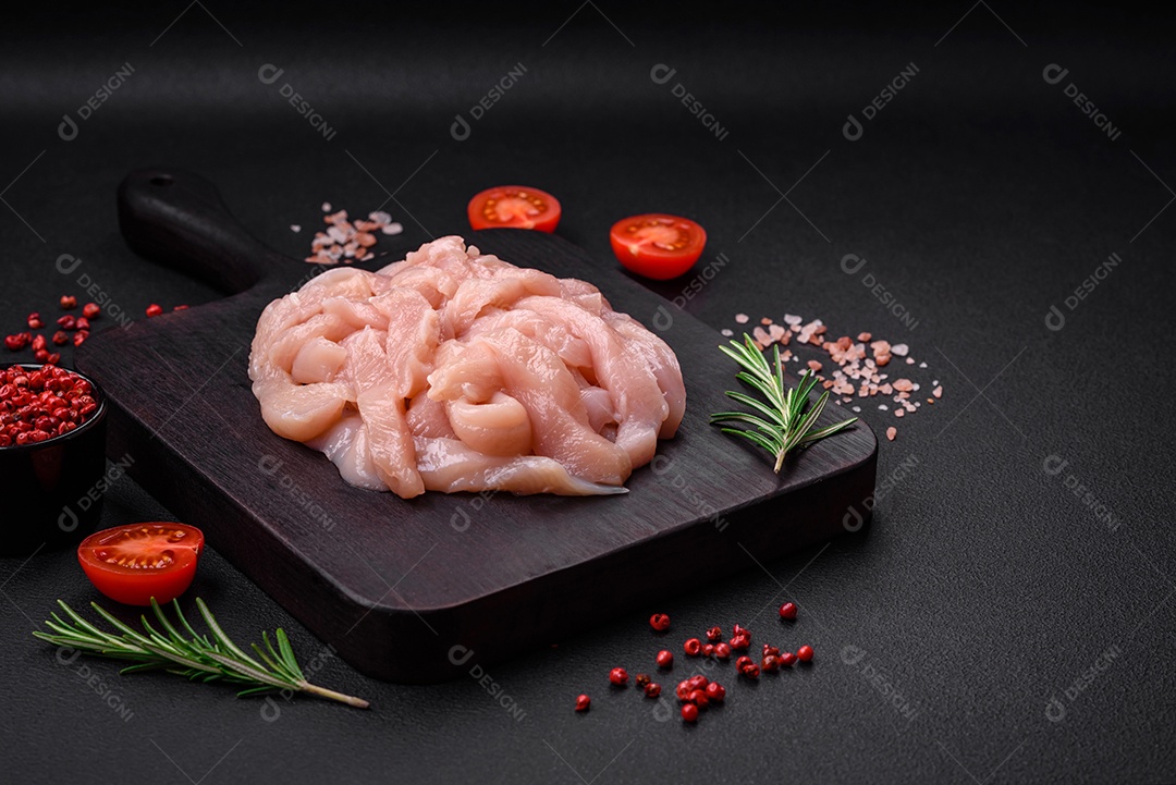 Filé de frango cru cortado em tiras com especiarias e ervas numa tábua de madeira