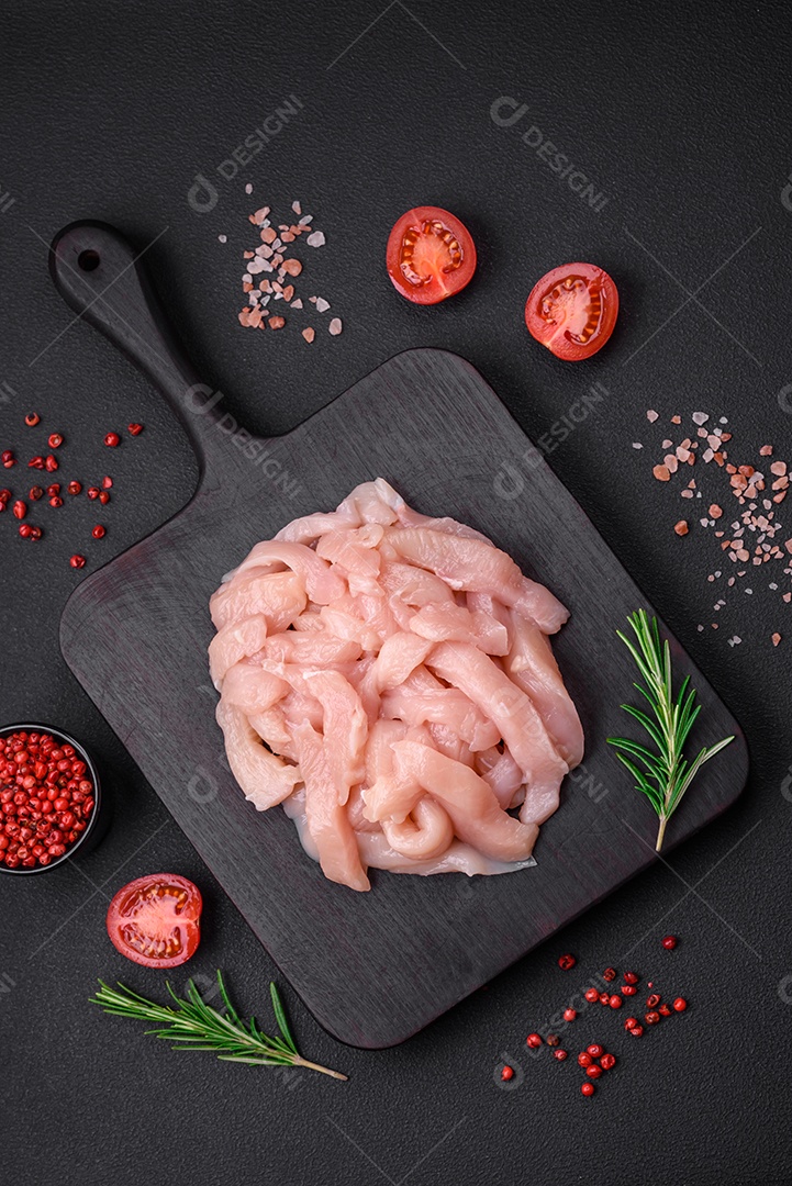 Filé de frango cru cortado em tiras com especiarias e ervas numa tábua de madeira