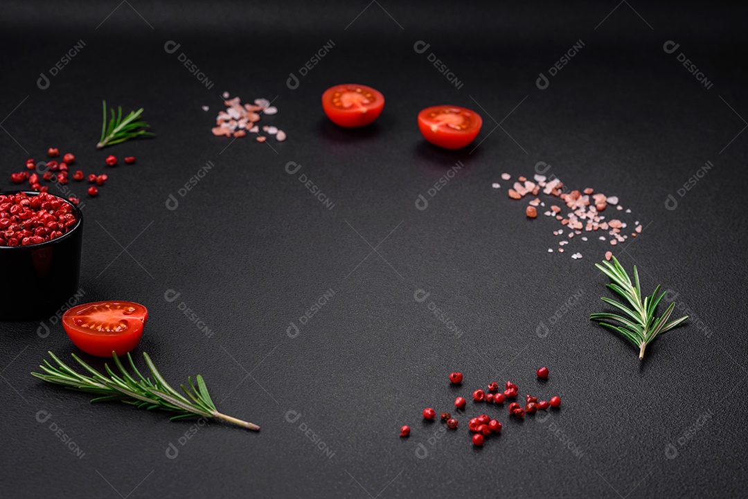 Especiarias, ervas e tomates sobre um fundo escuro.
