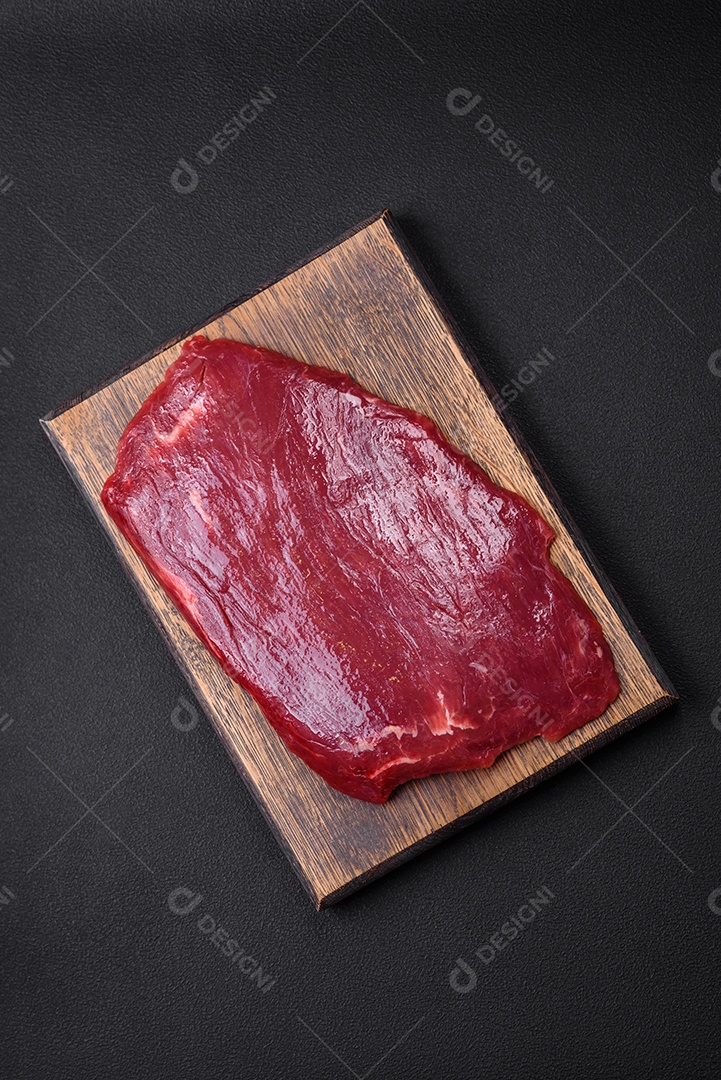 Carne crua fresca com sal, especiarias e ervas sobre um fundo escuro de concreto