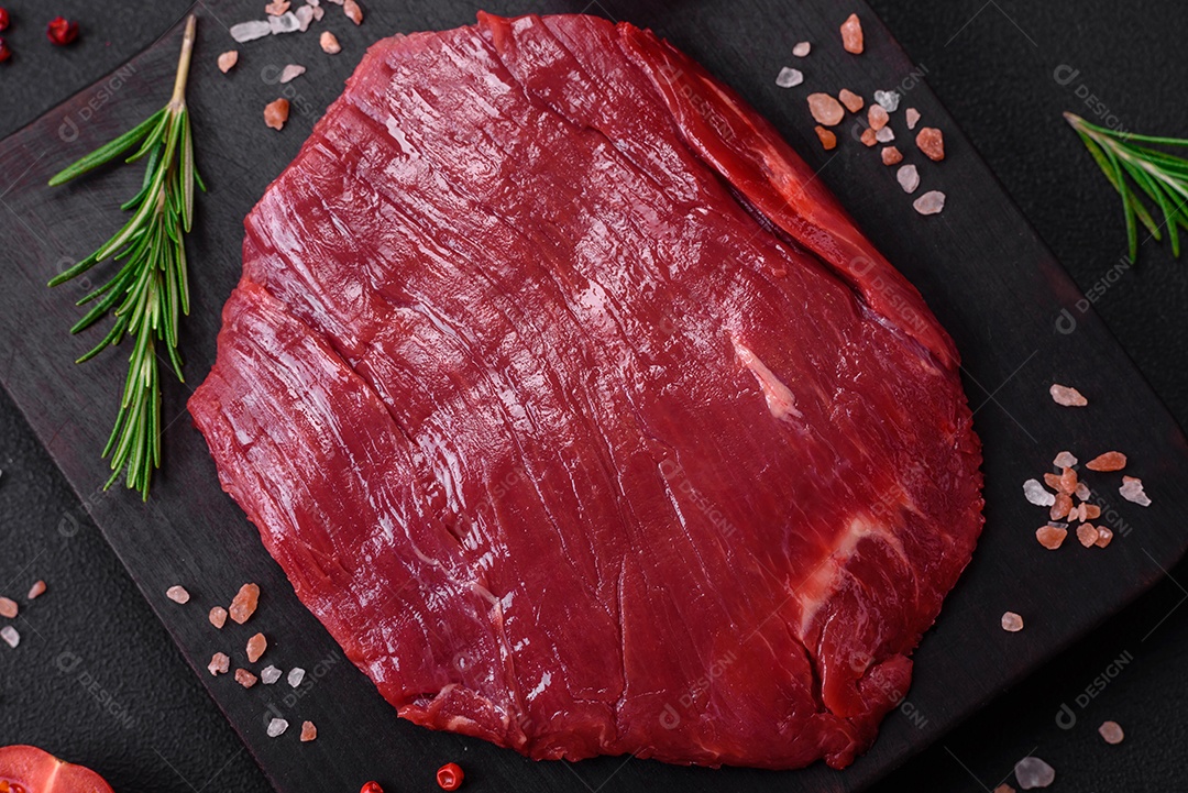 Carne crua fresca com sal, especiarias e ervas sobre um fundo escuro de concreto