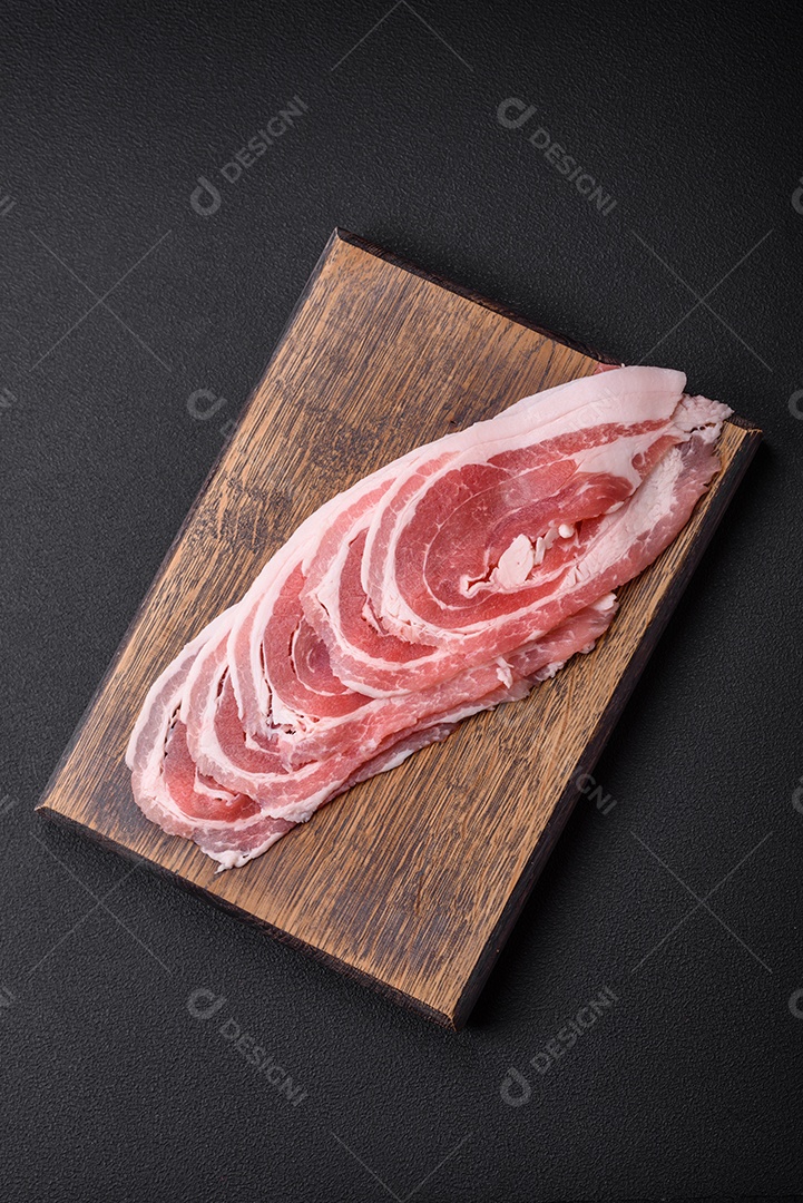 Bacon cru fresco cortado com especiarias e ervas sobre um fundo escuro de concreto