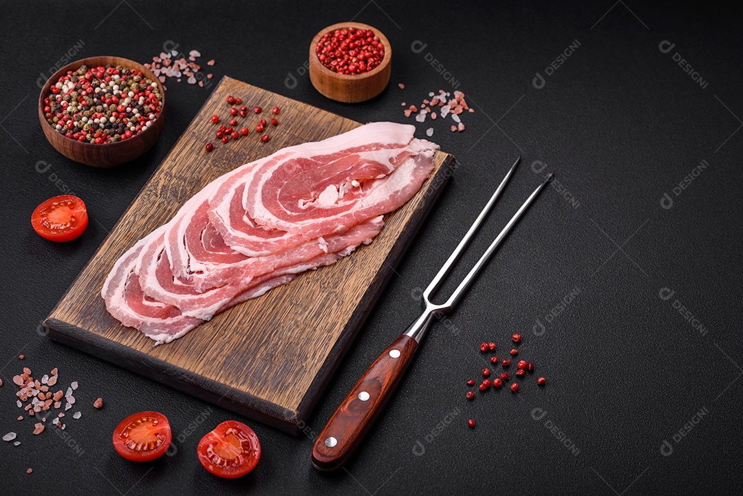 Bacon cru fresco cortado com especiarias e ervas sobre um fundo escuro de concreto