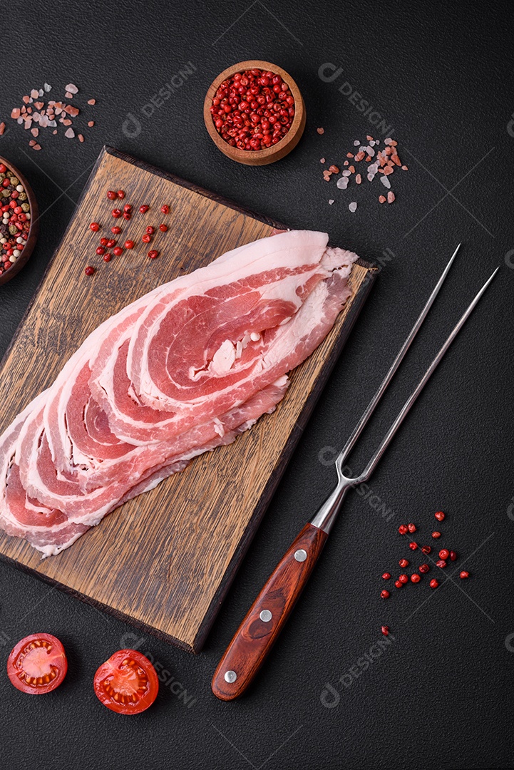 Bacon cru fresco cortado com especiarias e ervas sobre um fundo escuro de concreto