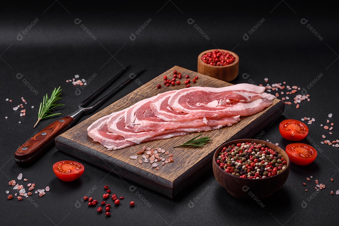 Bacon cru fresco cortado com especiarias e ervas sobre um fundo escuro de concreto