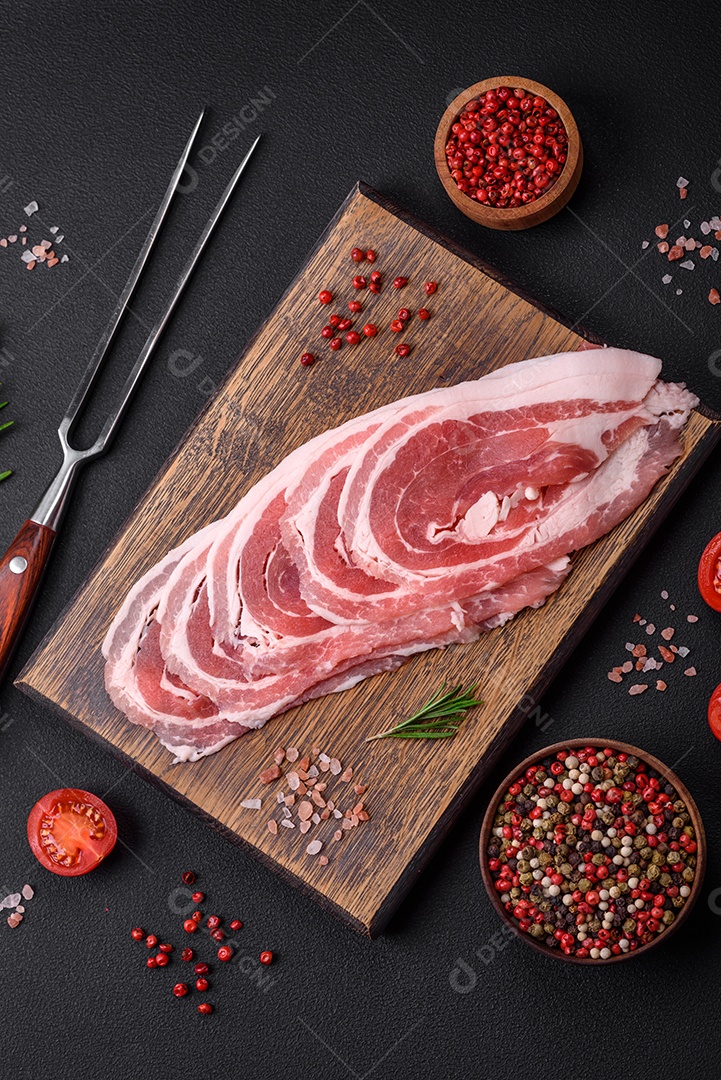 Bacon cru fresco cortado com especiarias e ervas sobre um fundo escuro de concreto