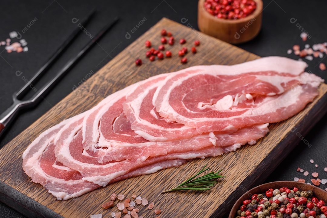 Bacon cru fresco cortado com especiarias e ervas sobre um fundo escuro de concreto