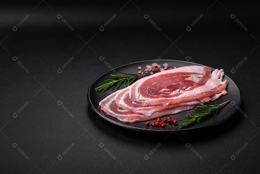 Bacon cru fresco cortado com especiarias e ervas sobre um fundo escuro de concreto