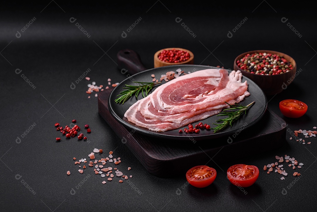 Bacon cru fresco cortado com especiarias e ervas sobre um fundo escuro de concreto