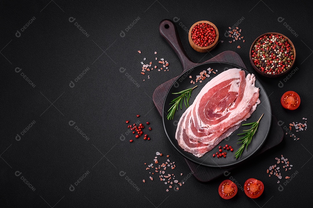 Bacon cru fresco cortado com especiarias e ervas sobre um fundo escuro de concreto
