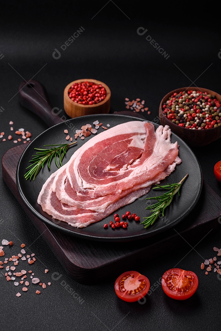 Bacon cru fresco cortado com especiarias e ervas sobre um fundo escuro de concreto