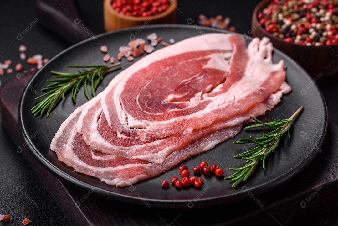 Bacon cru fresco cortado com especiarias e ervas sobre um fundo escuro de concreto
