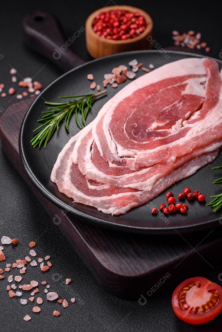 Bacon cru fresco cortado com especiarias e ervas sobre um fundo escuro de concreto