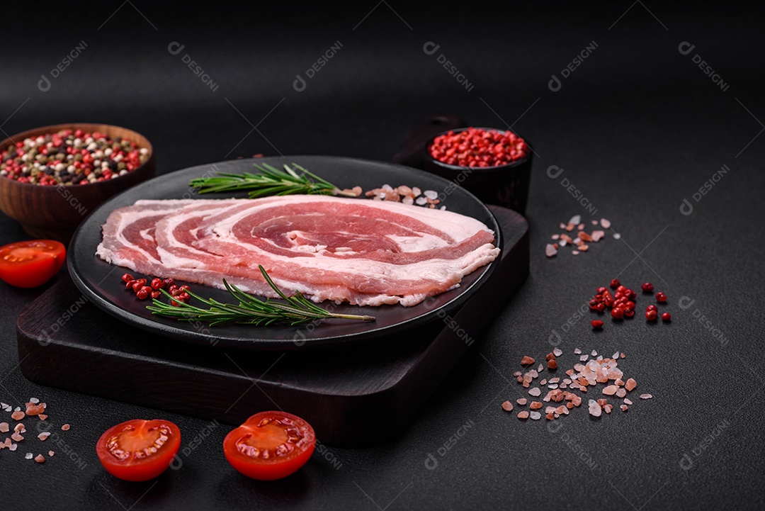 Bacon cru fresco cortado com especiarias e ervas sobre um fundo escuro de concreto
