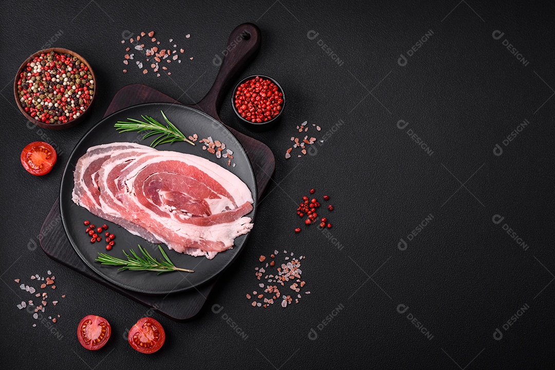 Bacon cru fresco cortado com especiarias e ervas sobre um fundo escuro de concreto