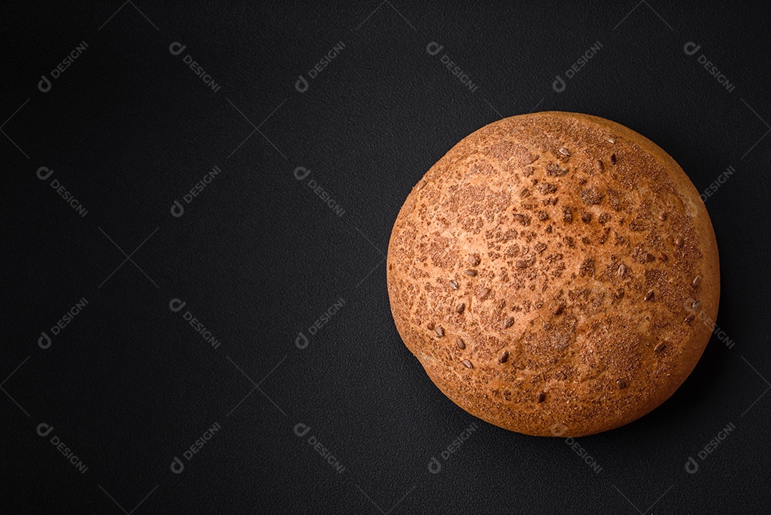Pão integral crocante fresco com sementes de gergelim e especiarias sobre um fundo escuro de concreto