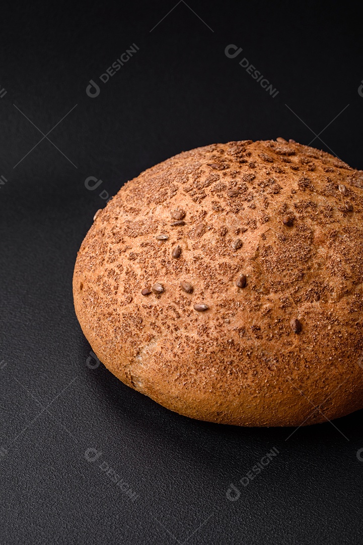 Pão integral crocante fresco com sementes de gergelim e especiarias sobre um fundo escuro de concreto