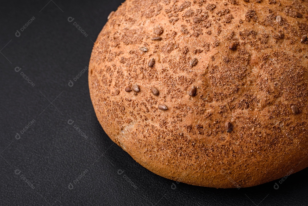 Pão integral crocante fresco com sementes de gergelim e especiarias sobre um fundo escuro de concreto