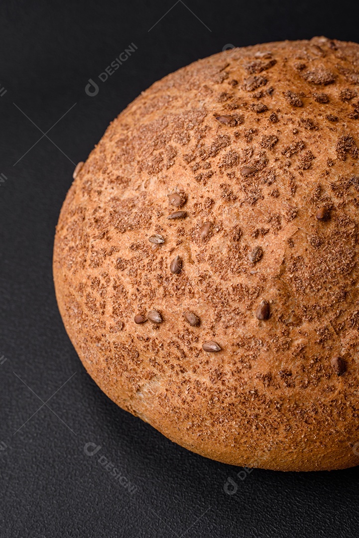 Pão integral crocante fresco com sementes de gergelim e especiarias sobre um fundo escuro de concreto