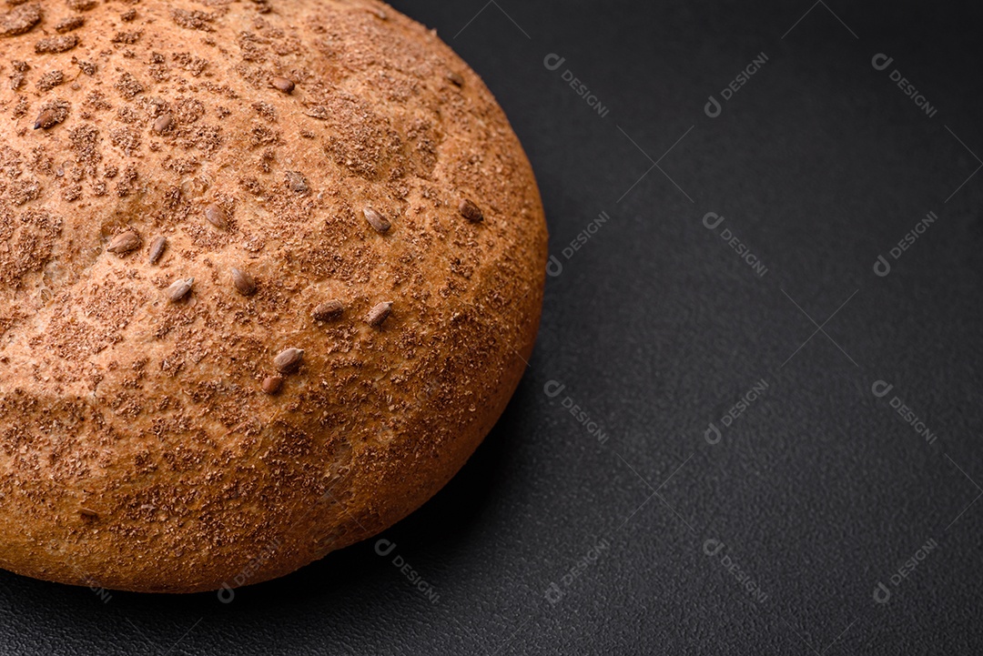 Pão integral crocante fresco com sementes de gergelim e especiarias sobre um fundo escuro de concreto