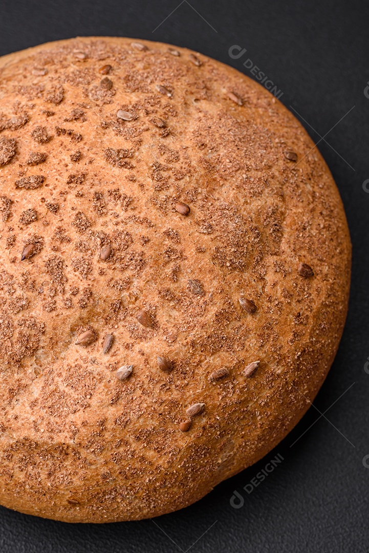 Pão integral crocante fresco com sementes de gergelim e especiarias sobre um fundo escuro de concreto