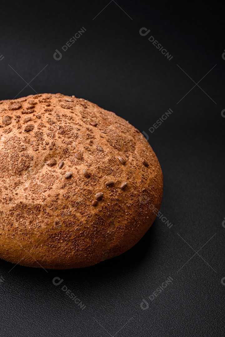 Pão integral crocante fresco com sementes de gergelim e especiarias sobre um fundo escuro de concreto